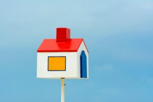 A vibrant birdhouse with red, yellow, and blue details set against a seamless blue sky.